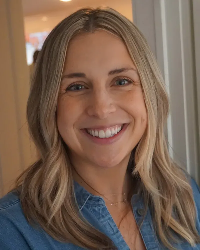 Carly Mulvey, smiling, standing by a French door