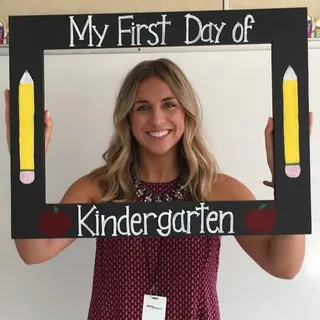 Carly on her first day teaching kindergarten, holding a My First Day of Kindergarten frame